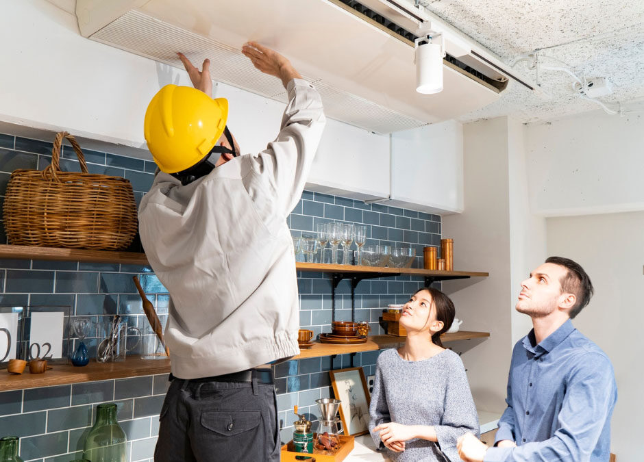 In a kitchen, a man and woman are standing together under a ceiling fan, engaged in conversation.